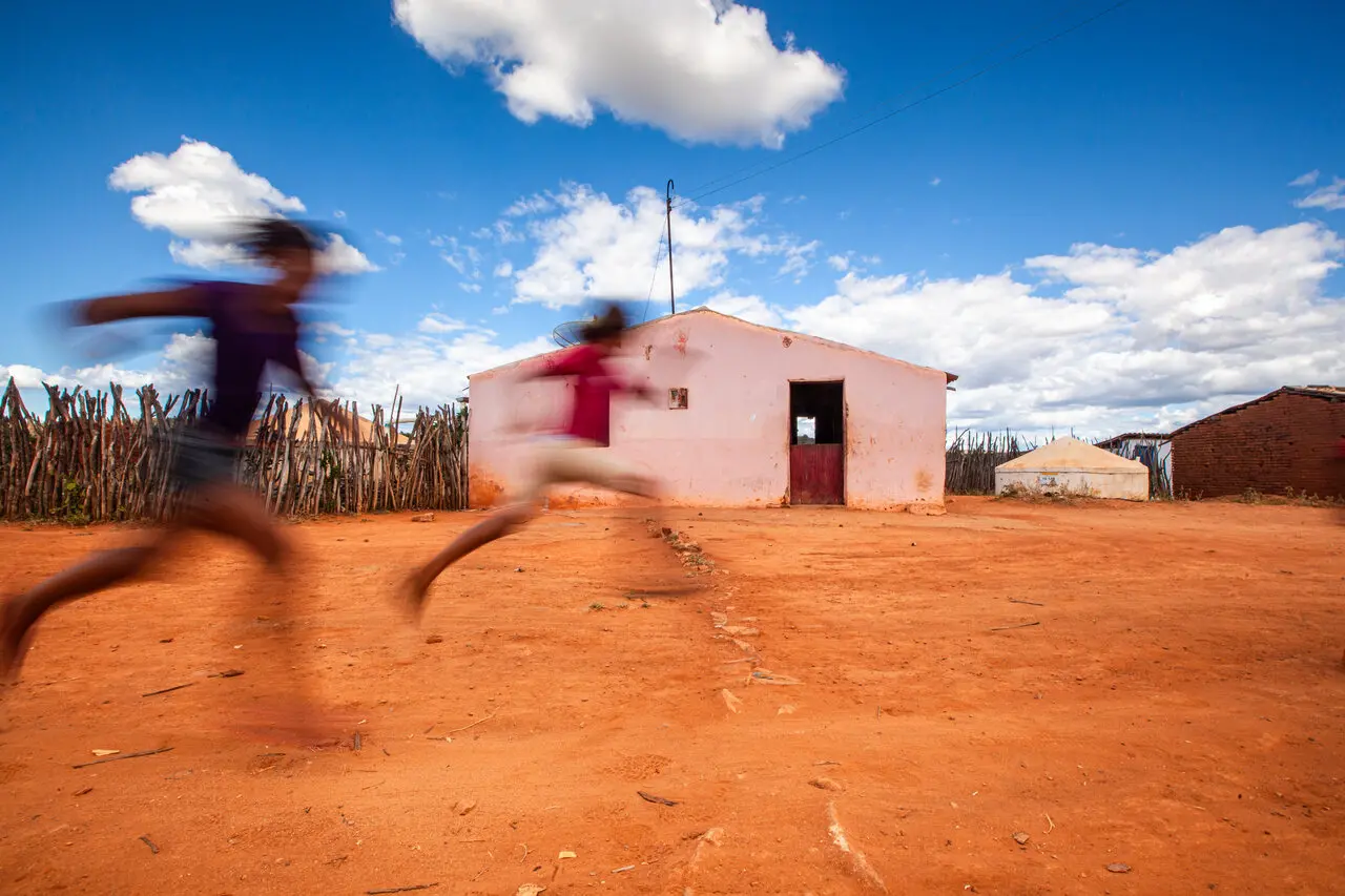 Fotografia de crianças correndo em frente a uma pequena casa no Cariri cearense