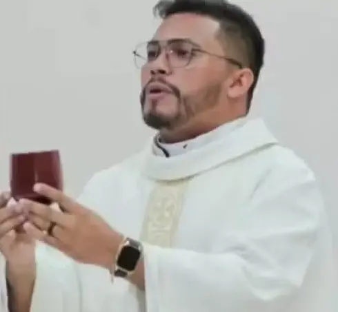 Padre Paulo segurando um cálice de vinho. Ele usa óculos de armação fina e tem barba bem aparada