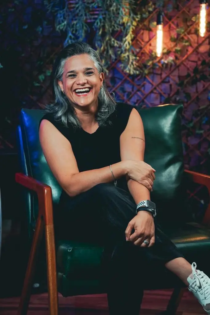 Jassy Ribeiro é uma mulher de cabelos lisos e grisalhos e, na foto, está usando roupas pretas. Ela está sorrindo