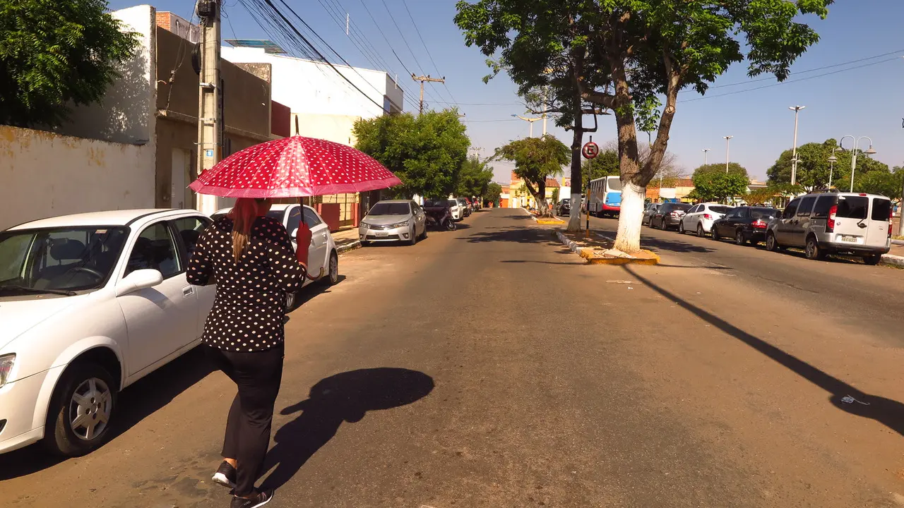 Mulher anda na rua com guarda-chuvas para se proteger do sol