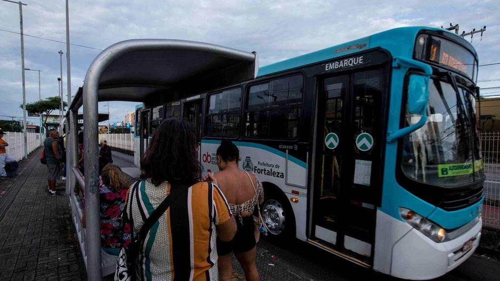 Foto de pessoas na parada de ônibus, ao lado de um ônibus