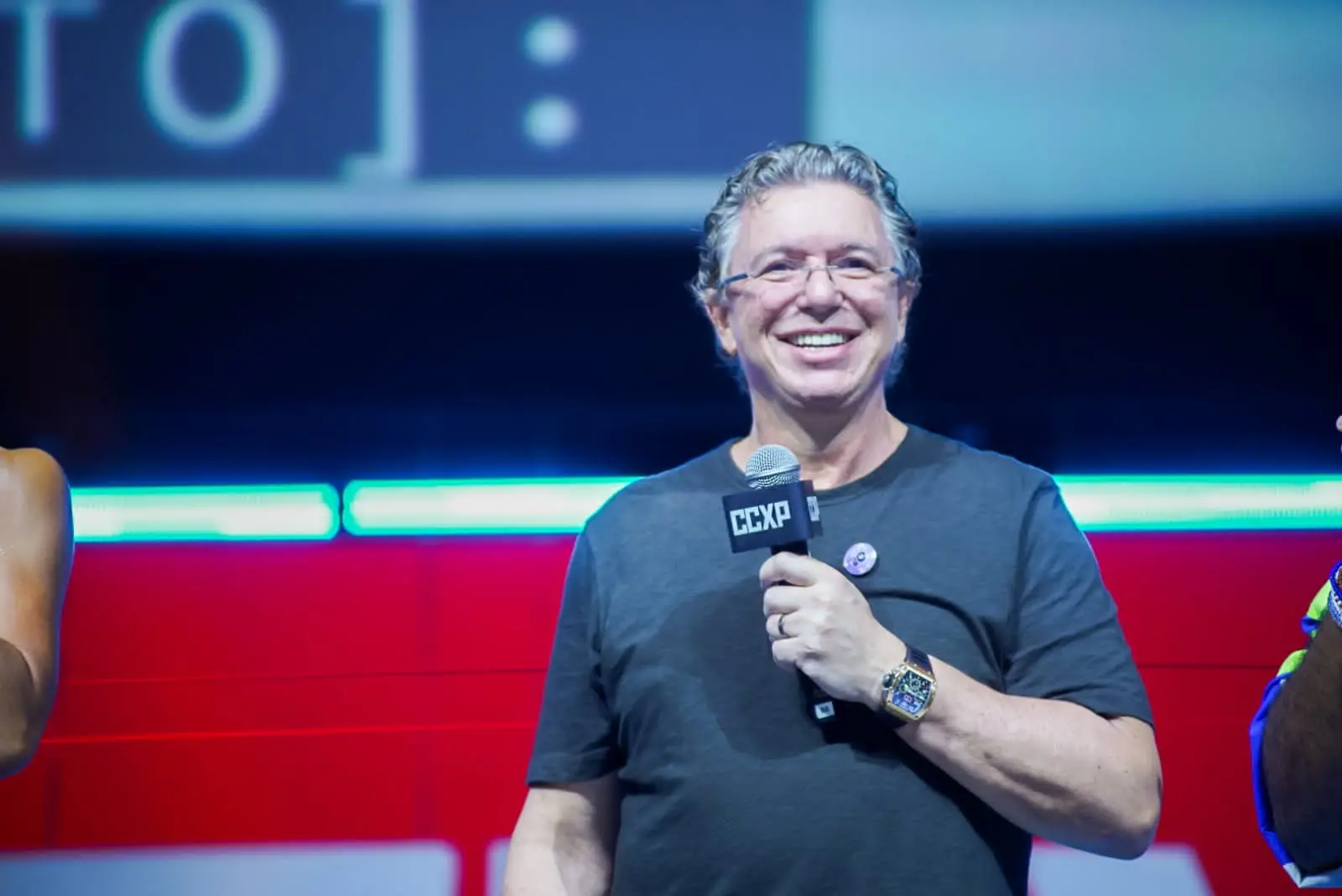 Boninho segura um microfone enquanto discursa em painel. Ele é um homem branco e de cabelos ondulados também brancos