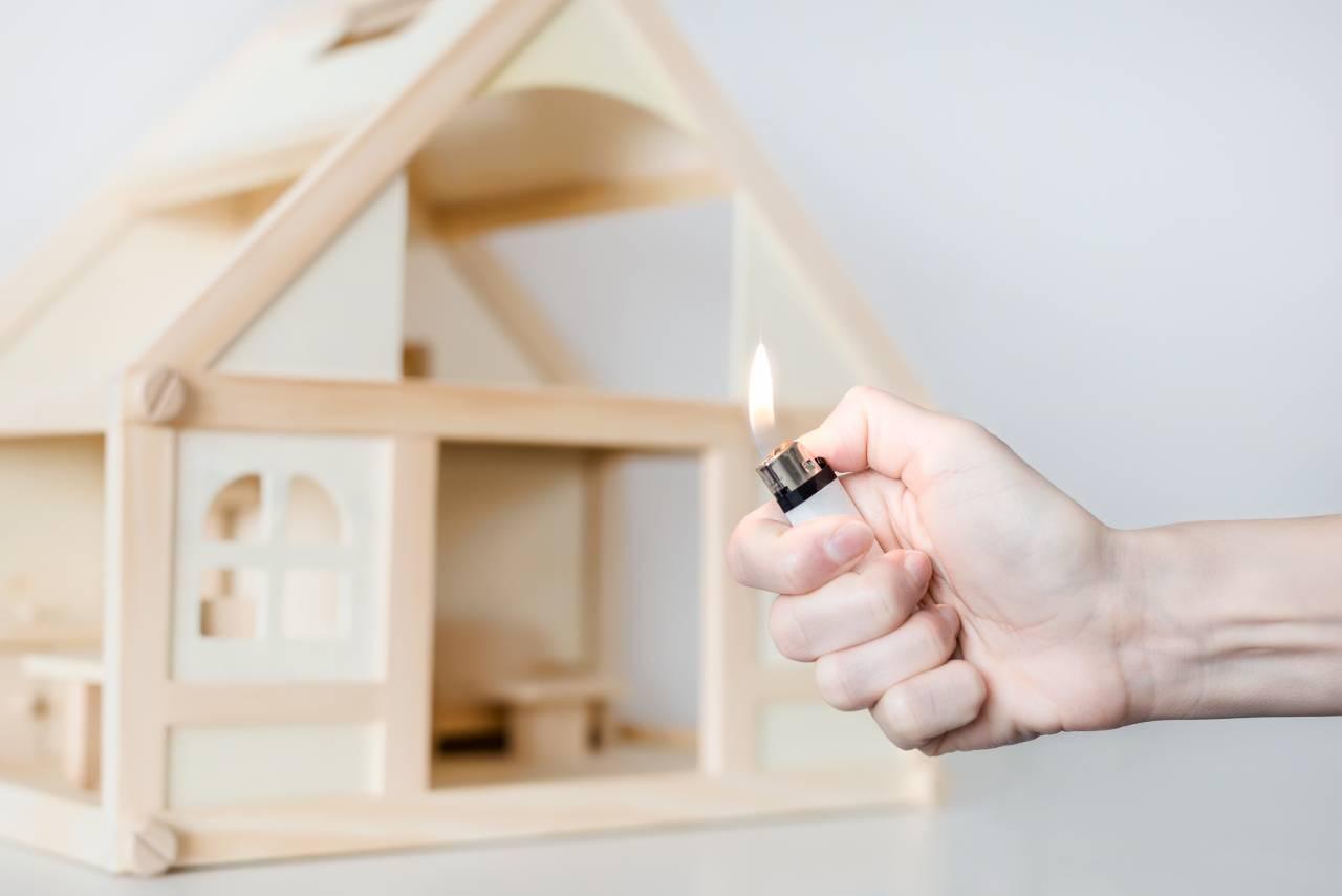 Mão segura isqueiro aceso em frente a casinha de madeira