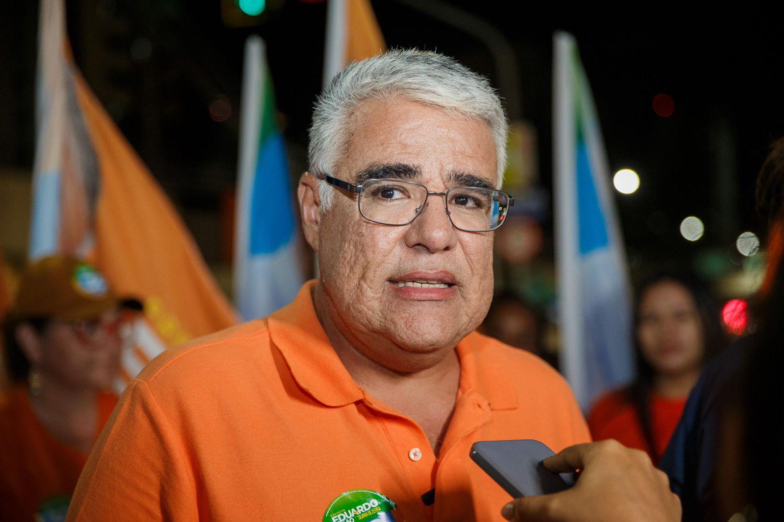 Eduardo Girão é um homem branco de cabelo grisalho. Na foto, ele está de camisa polo laranja e usa óculos de grau