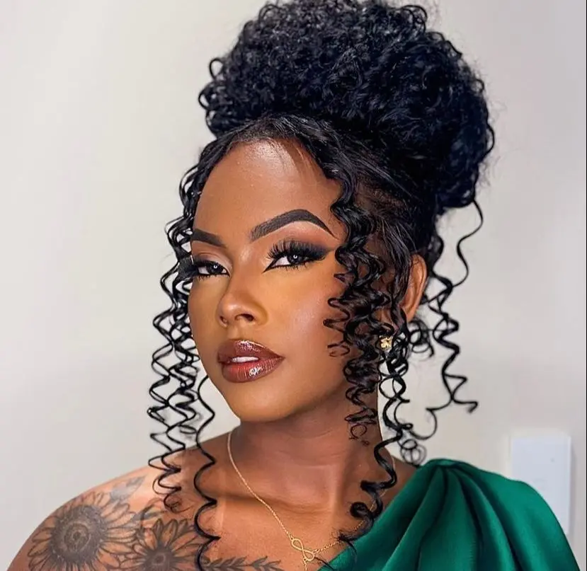 Monique é uma mulher negra jovem. Na foto, ela está maquiada e com o cabelo cacheado amarrado em um coque