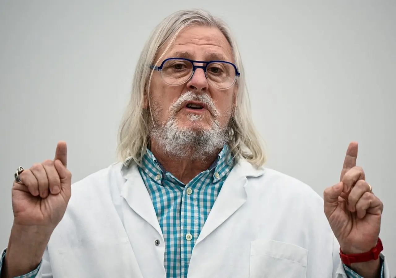Imagem mostra um homem branco de cabelos longos e jaleco. Ele está gesticulando.