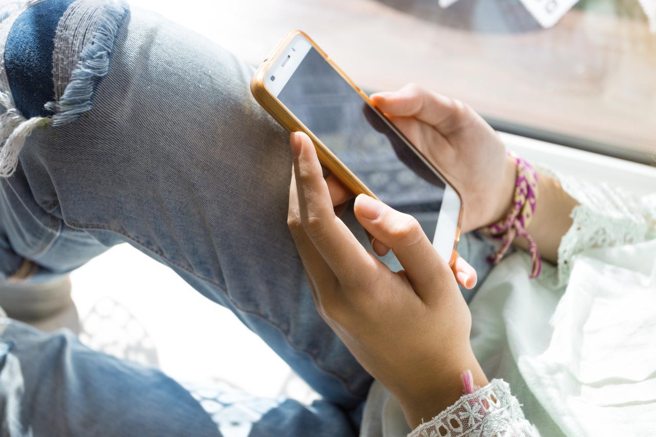 Jovem com celular nas mãos, rosto não aparece