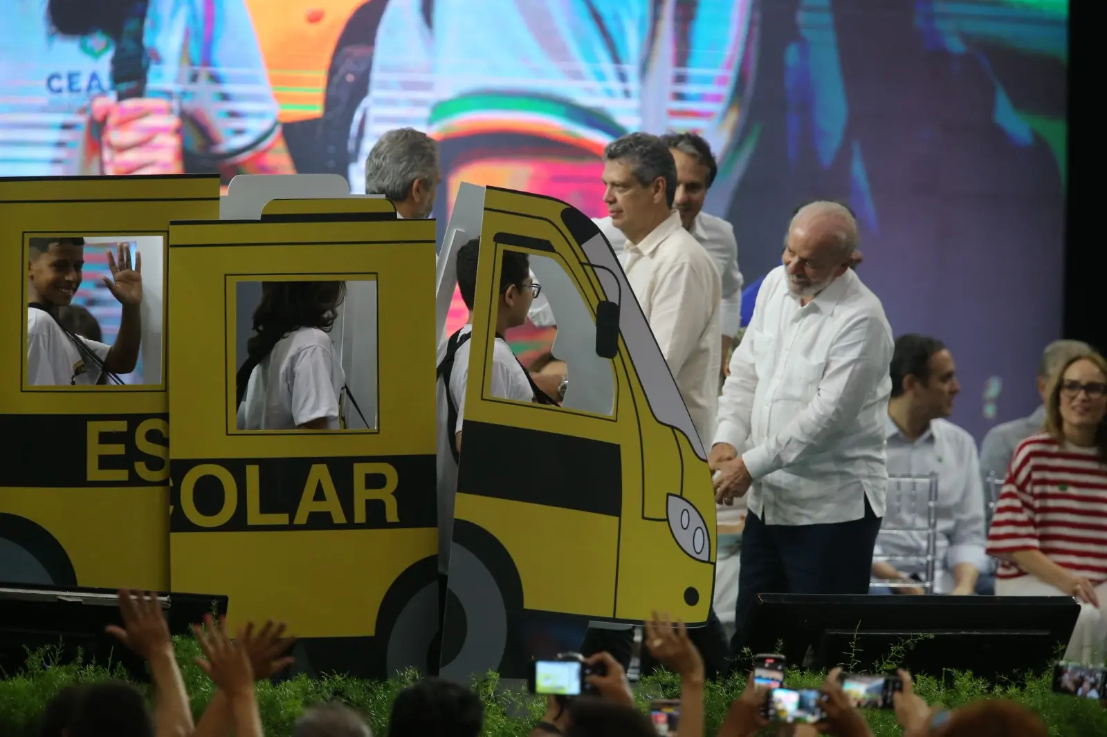 O presidente Lula observa alunos que estão em uma representação de um ônibus escolar