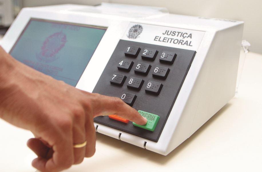 Mão de eleitor pressionando a tecla confirma na urna eletrônica
