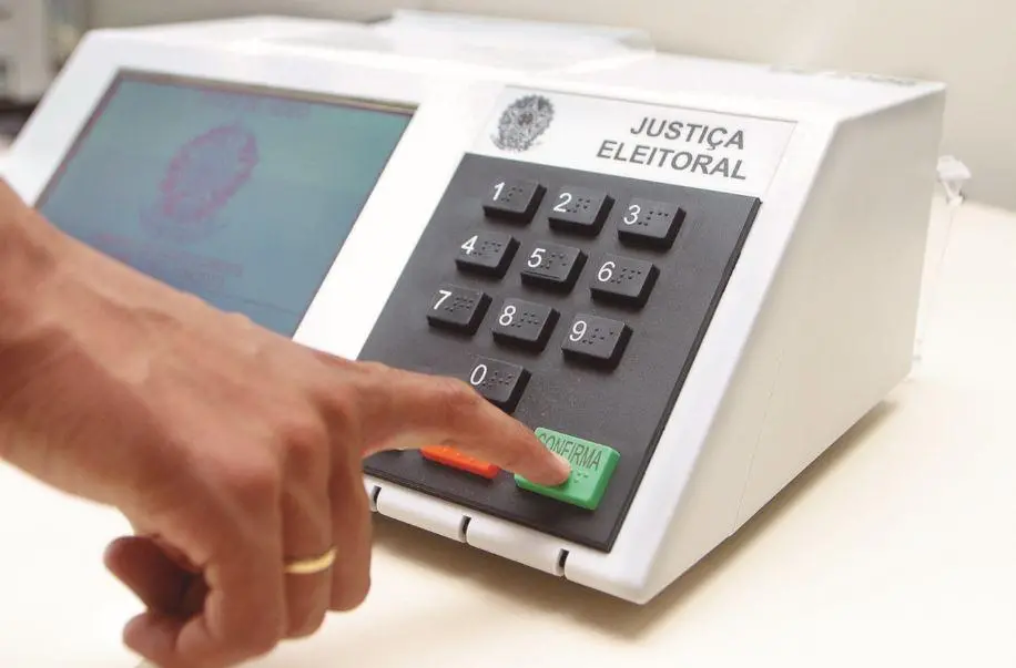 Mão de eleitor pressionando a tecla confirma na urna eletrônica