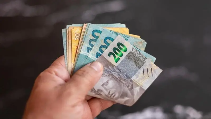 foto de pessoa segurando cédulas de 100 200 e 20 reais.