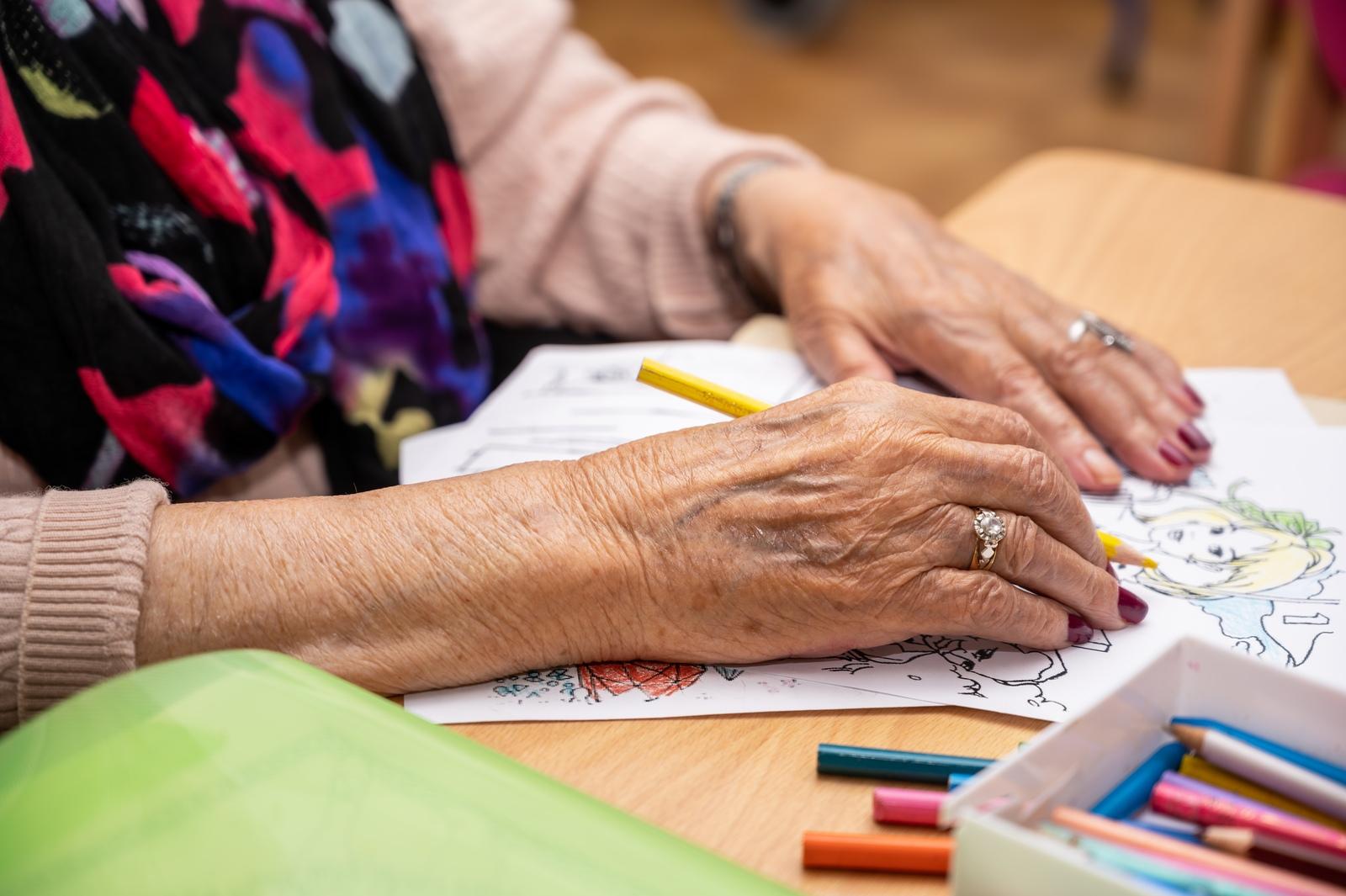 Mãos de pessoa idosa pintando desenho com lápis de cor