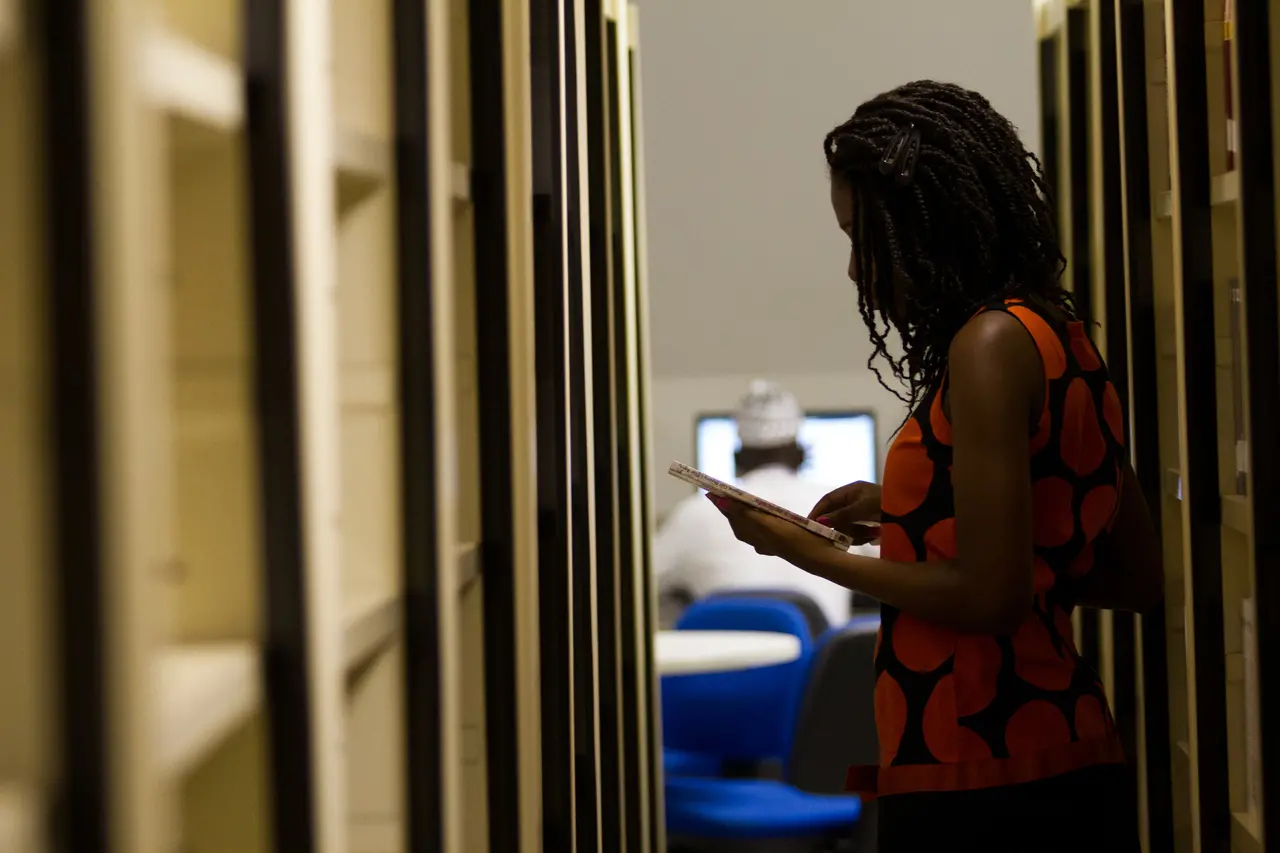 Silhueta de uma estudante estrangeira da Unilab de lado, folheando um livro na biblioteca