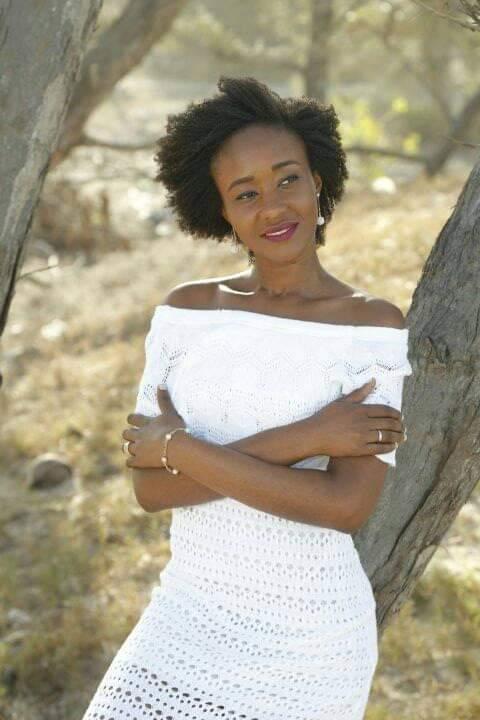 Nené Inturé, Verinha, mulher de Guiné-Bissau, usando vestido branco e com os braços cruzados, como em um abraço, olhando para o lado direito