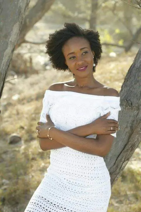 Nené Inturé, Verinha, mulher de Guiné-Bissau, usando vestido branco e com os braços cruzados, como em um abraço, olhando para o lado direito