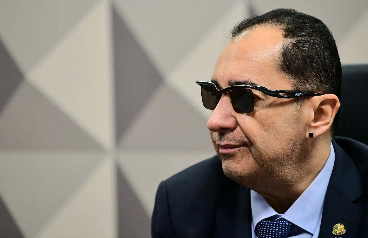 O senador Jorge Kajuru é um homem de meia idade e na foto está de óculos escuros, terno preto, camisa social azul e gravata azul