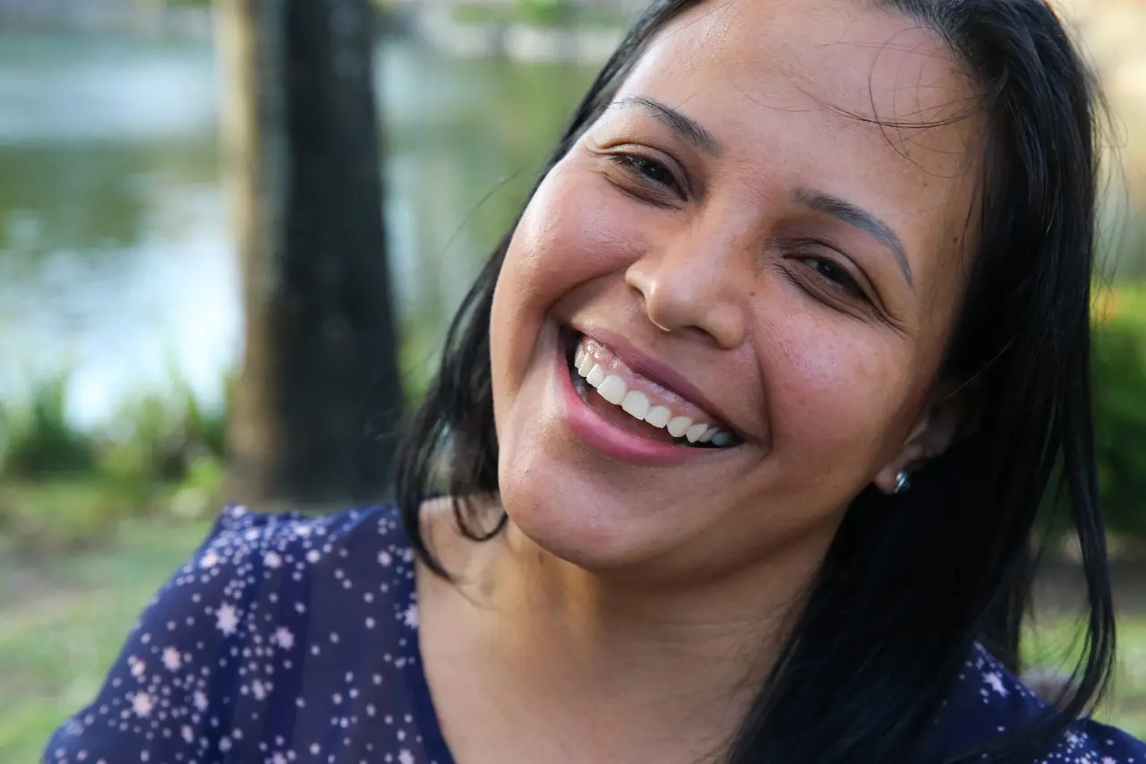 Retrato com foco no rosto de Eimily, mulher venezuelana de cabelos pretos e lisos, sorrindo para a câmera