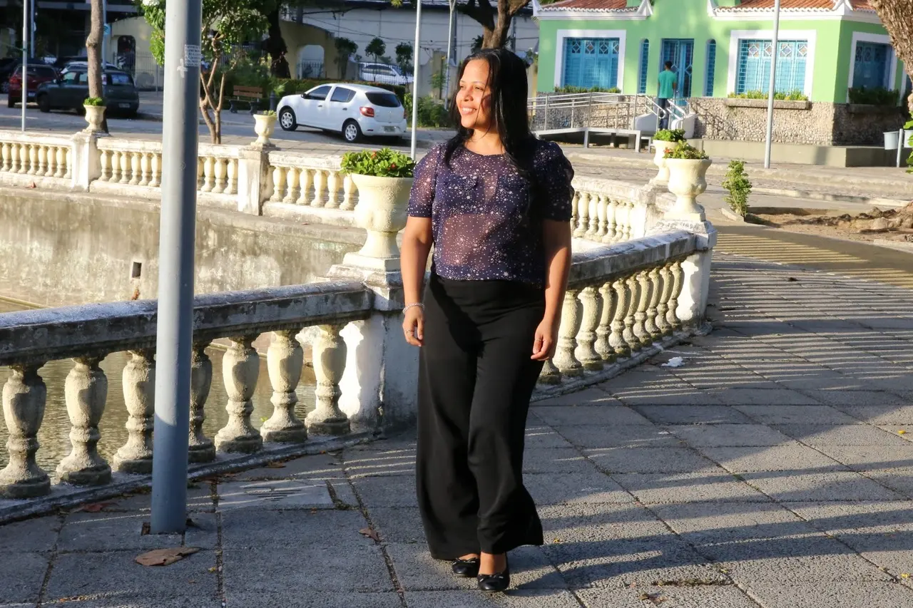 Mulher vestida de blusa roxa com transparência e calça preta caminha em parque de Fortaleza