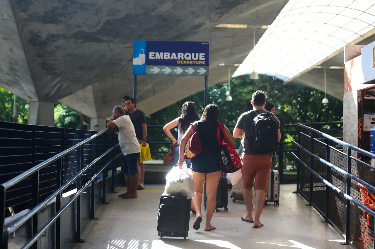 Passageiros caminhando na rodoviária de Fortaleza, em frente a placa onde está escrito 