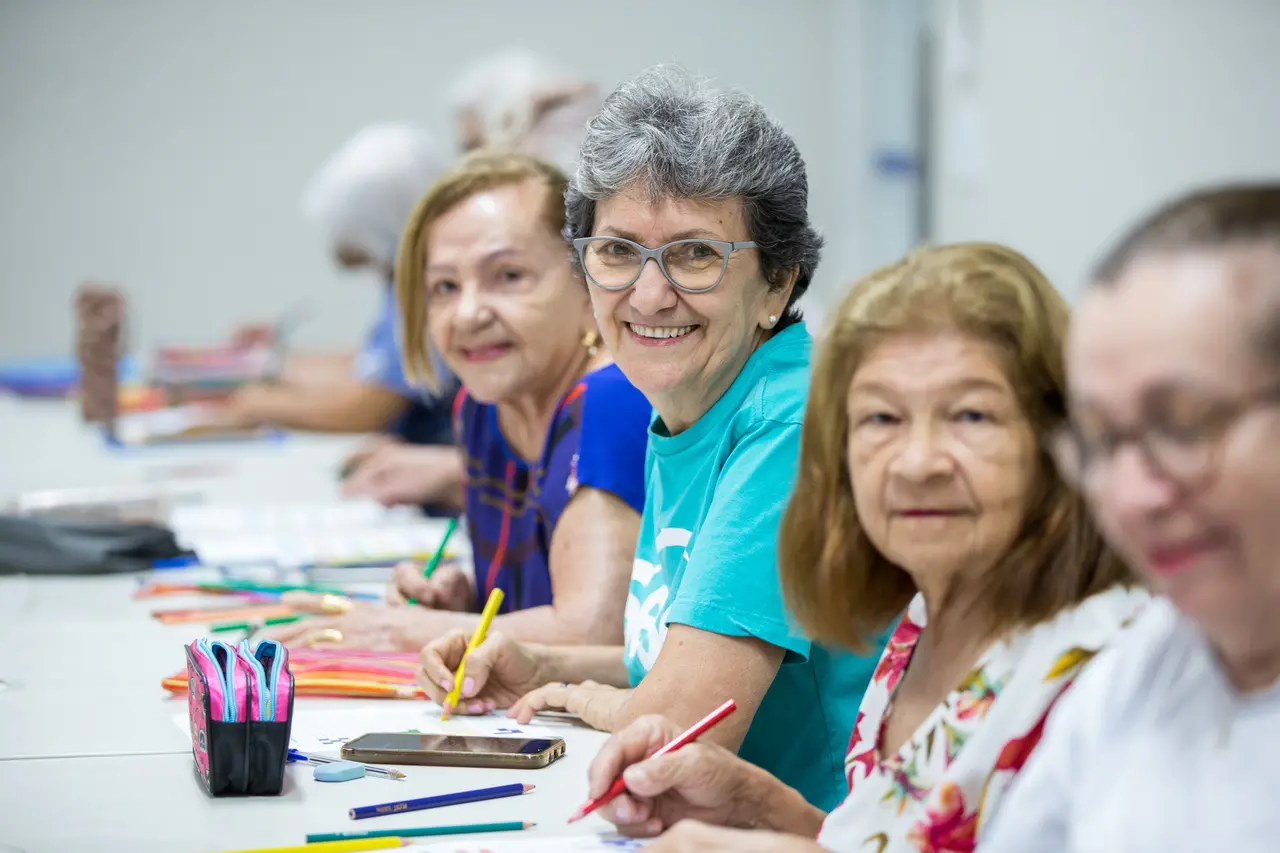 Quatro mulheres mais velhas fazendo atividade de terapia ocupacional. Uma delas, de blusa azul, está em foco. As outras estão desfocadas.