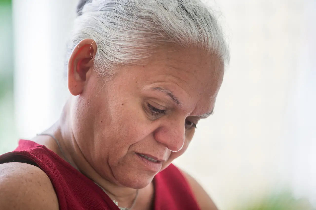 Nilde, uma mulher de cabelos brancos e usando vestido vermelho, de cabeça baixa