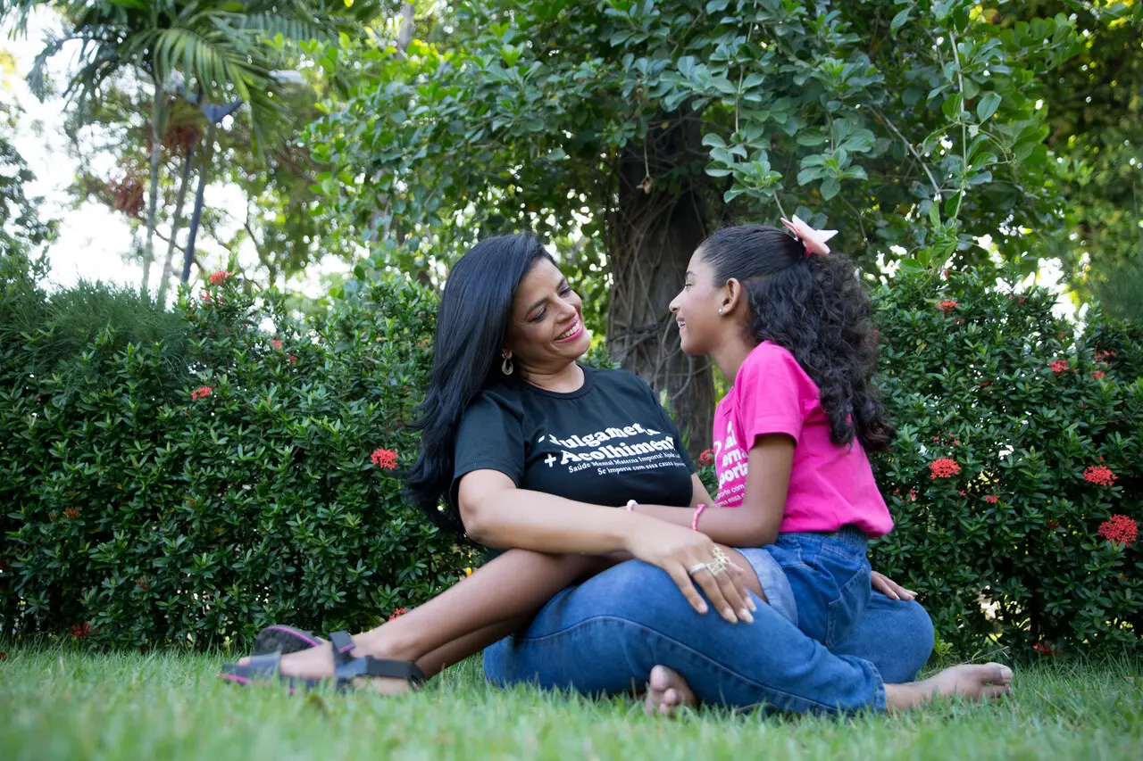 Ghislayne Paiva e a filha Joana, sentadas na grama de uma praça