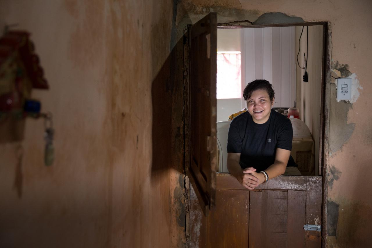 Brena encostada na porta, cuja metade de baixo está fechada e a de cima, aberta