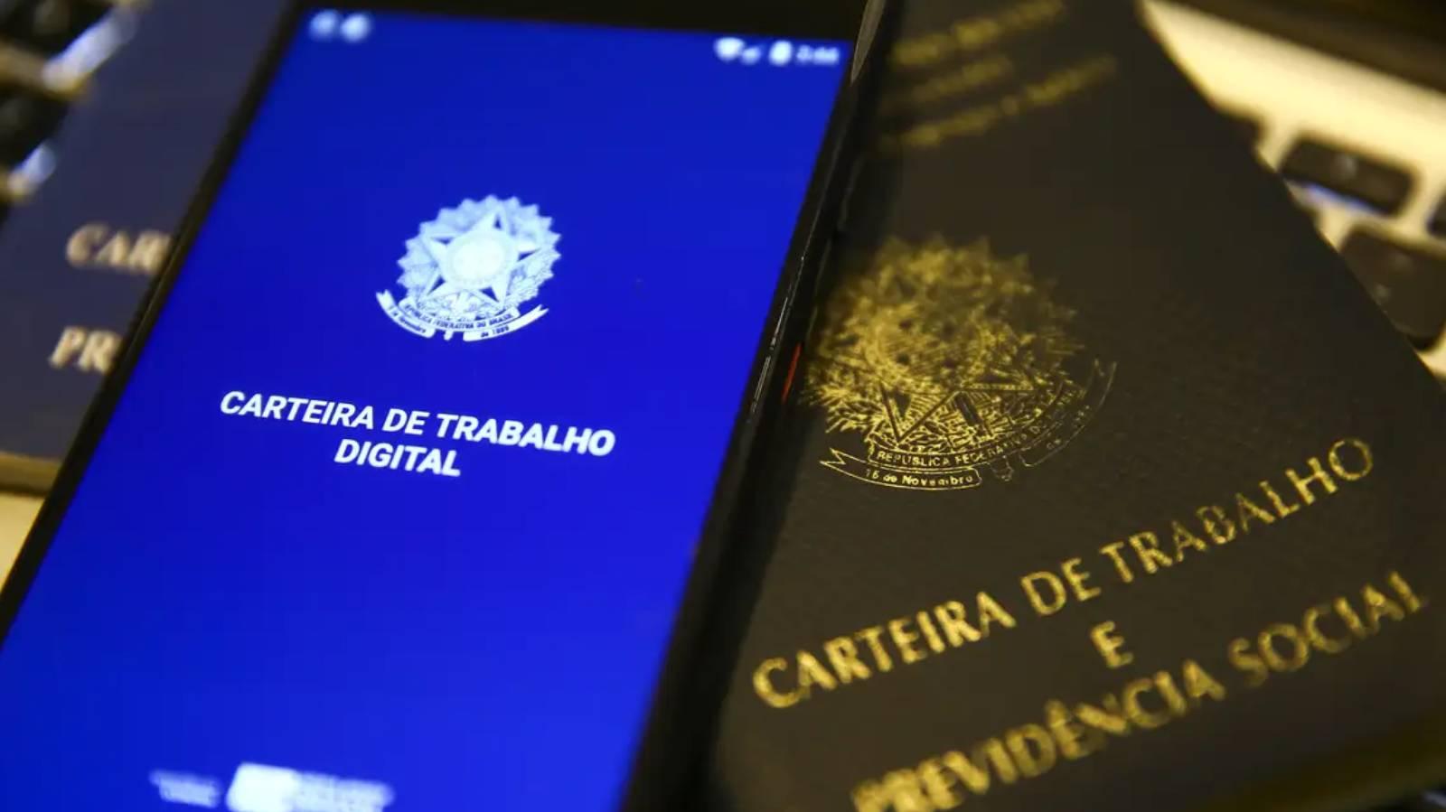 Foto mostra um celular com o aplicativo da carteira de trabalho digital aberto em cima de carteira de trabalho física. Segunda menor taxa de desemprego