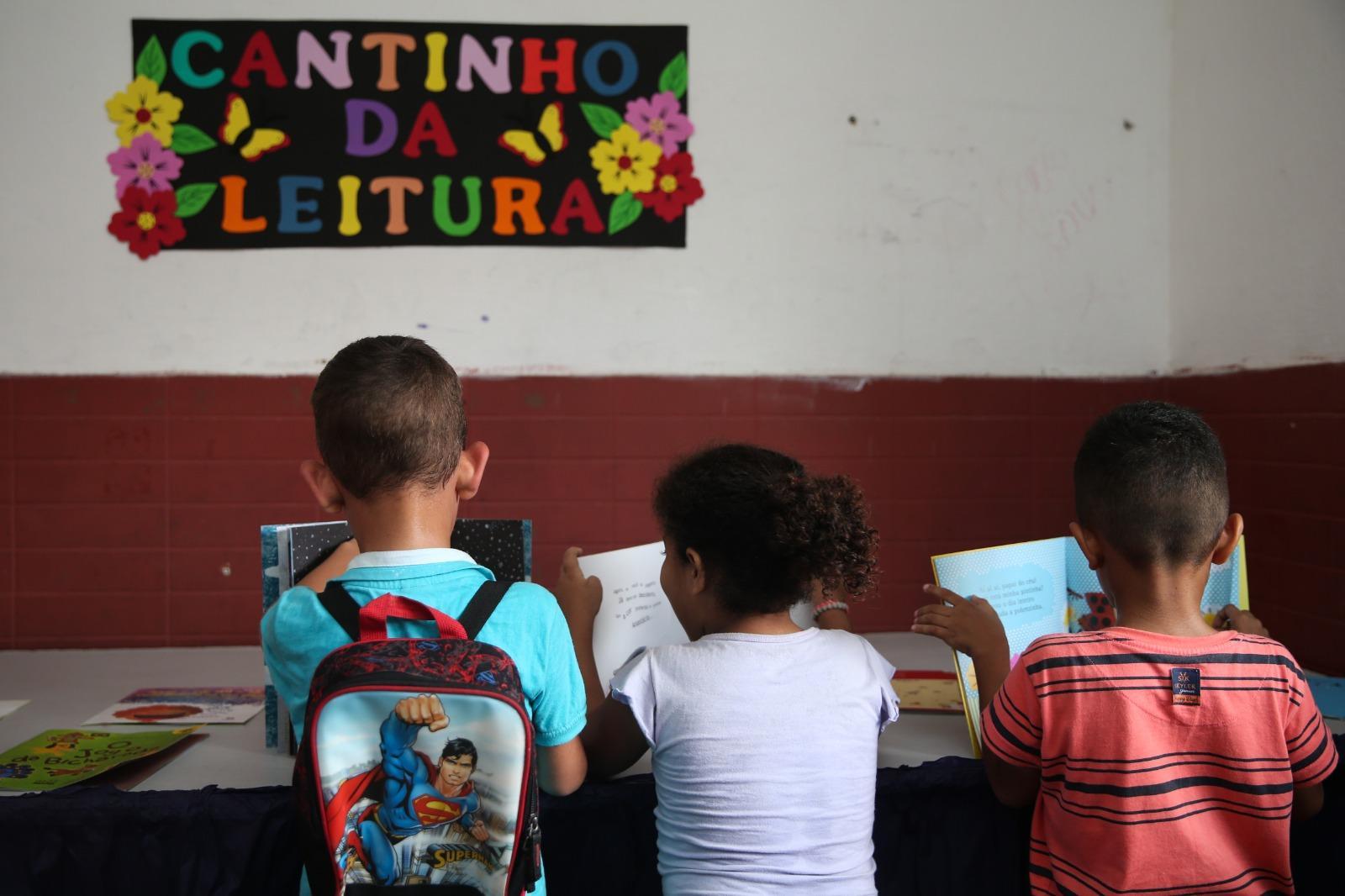 Três crianças de costas, com livros nas mãos, no Cantinho da Leitura