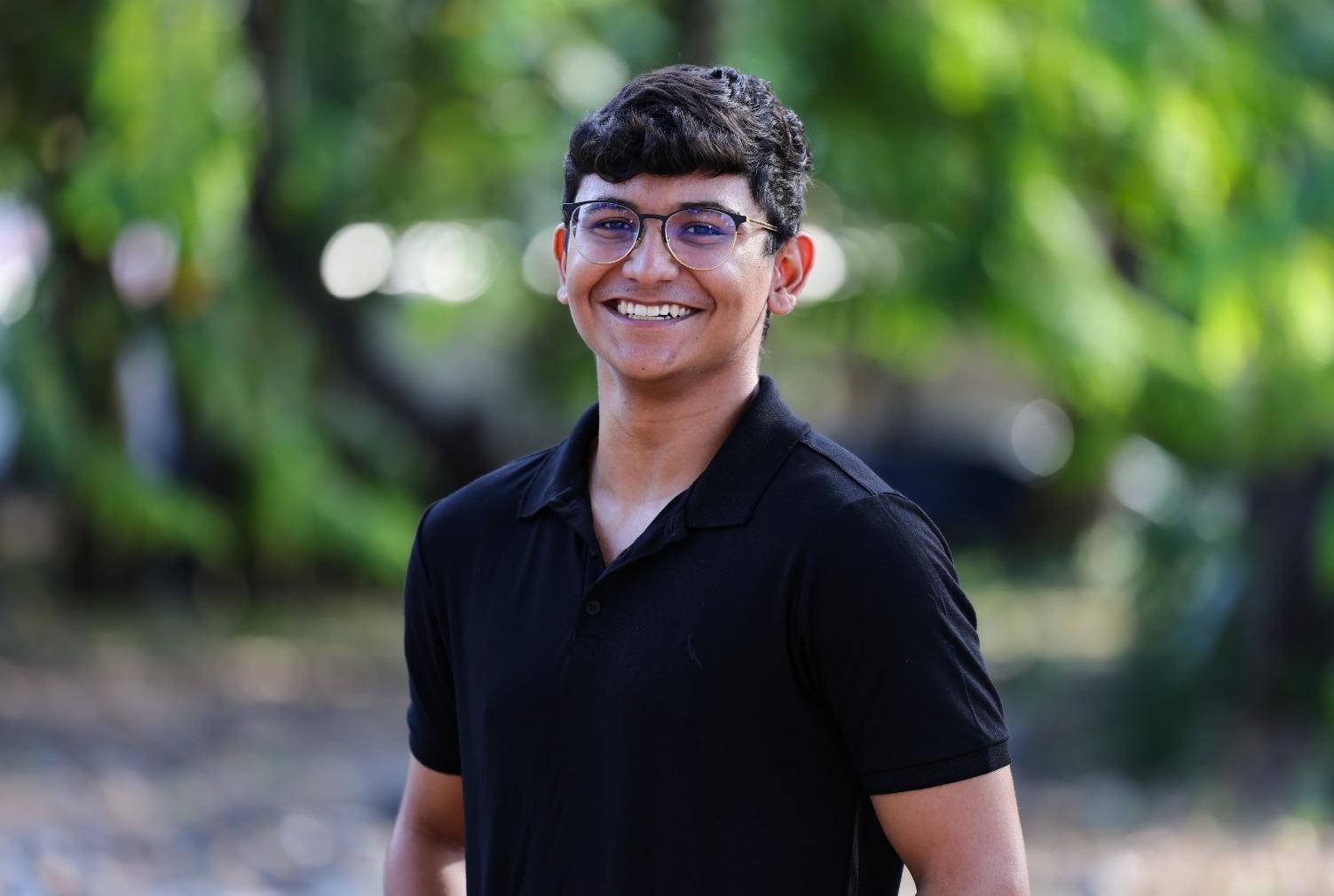 Miguel é um jovem negro de cabelo curto preto e usa óculos de grau. Na foto, ele está de camisa gola polo preta