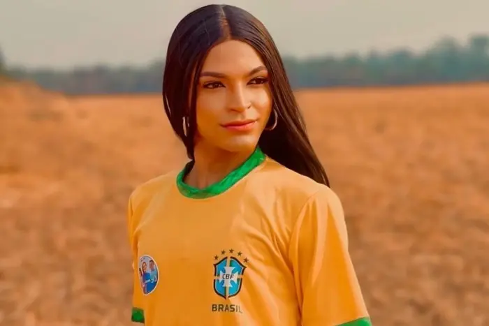 Cantora e suplente de vereadora SantRosa é uma mulher trans de cabelo preto longo e liso. Na foto, ela está com camisa verde e amarela da seleção brasileira