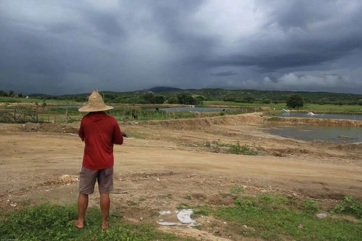 Homem de chapéu de palha, de costas para a foto, olhando para um rio seco no Ceará