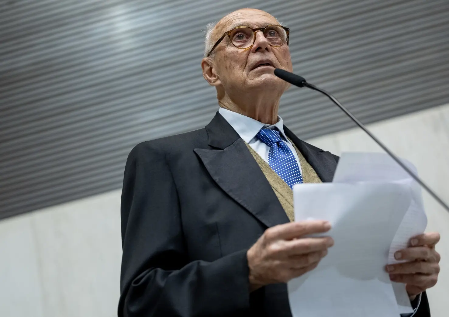 Suplicy é um homem idoso, branco, magro e com poucos fios de cabelos brancos. Na foto, ele está de terno preto, pulover marrom, camisa social branca e gravata azul. Além disso, usa óculos de grau