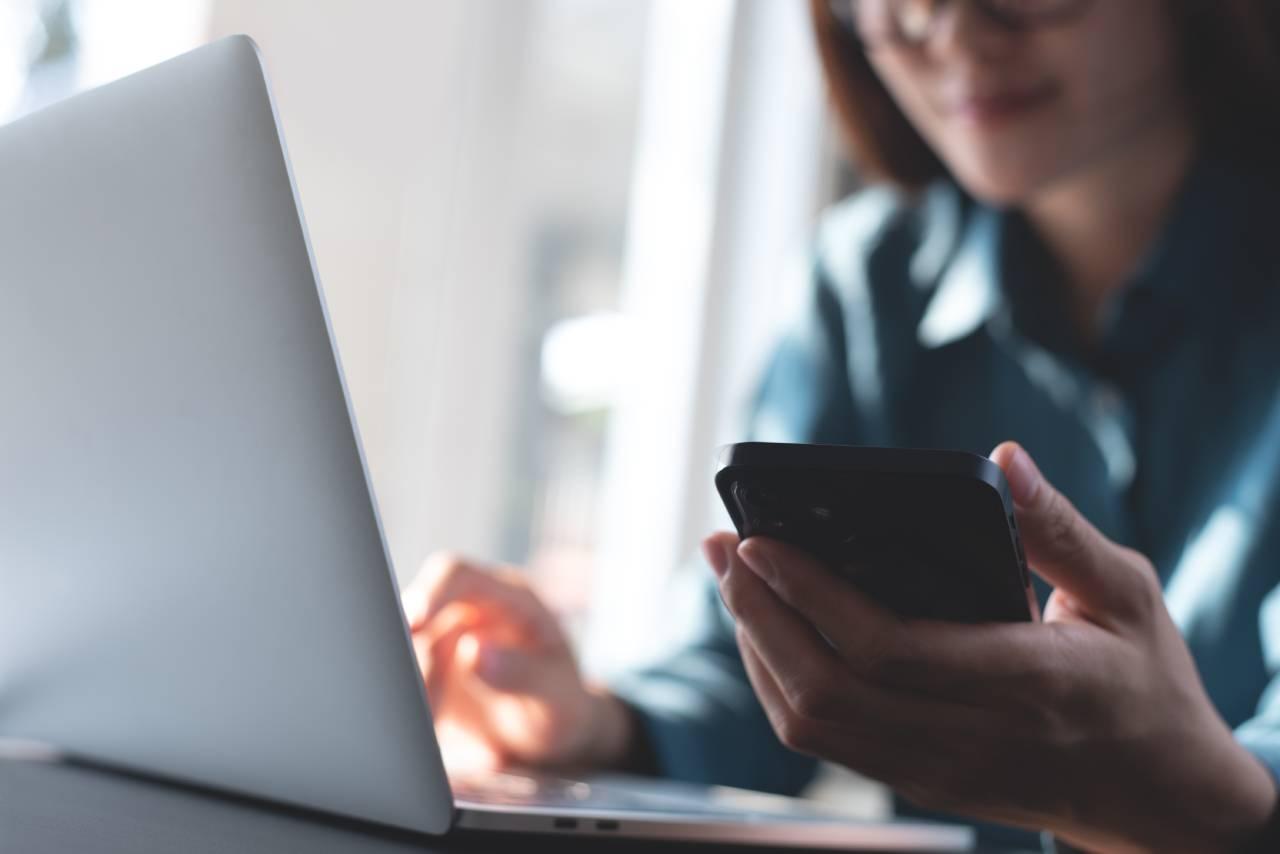 Mulher segurando celular em frente a notebook