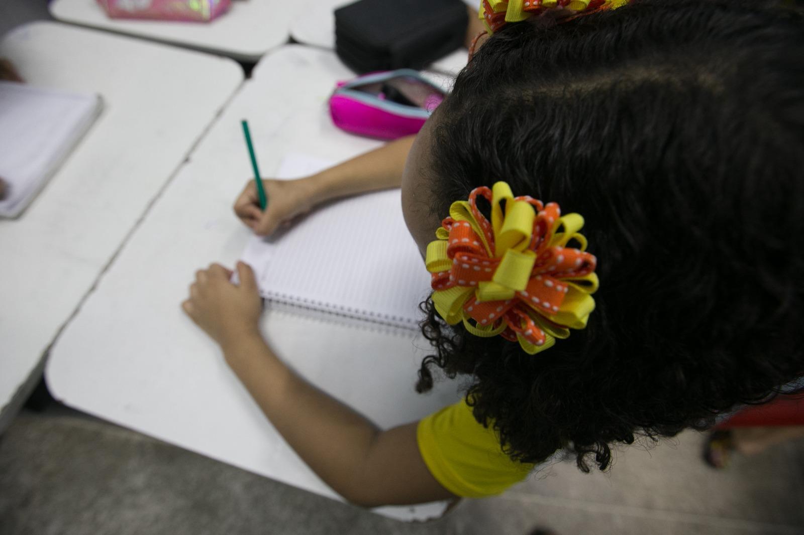 criança do ensino fundamental em uma carteira escolar escrevendo