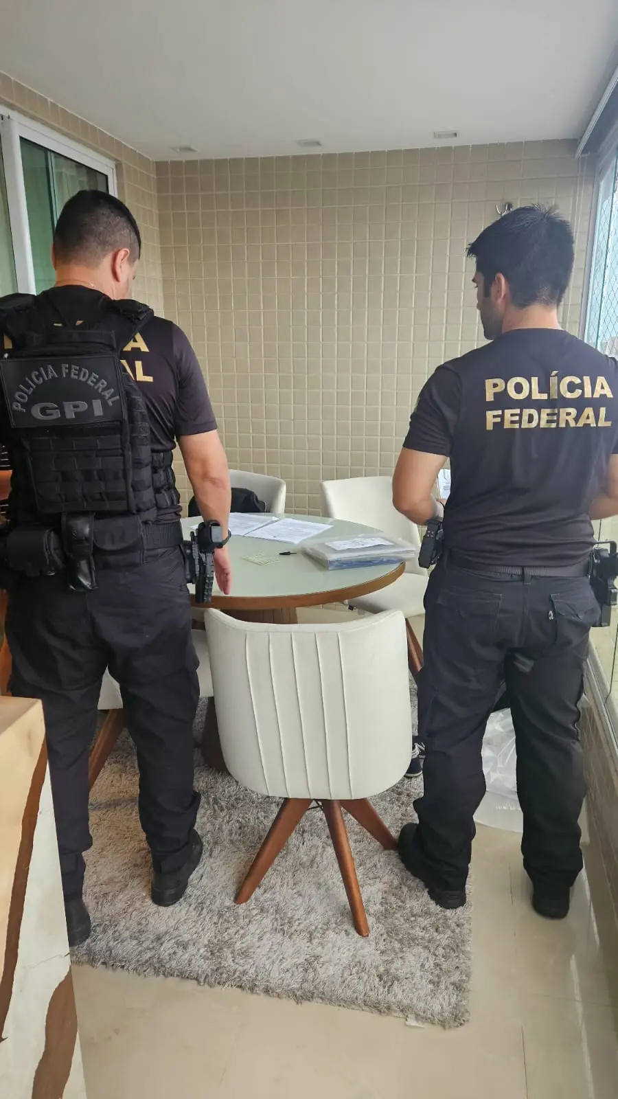 policiais federais de costas diante de mesa cheia de papéis