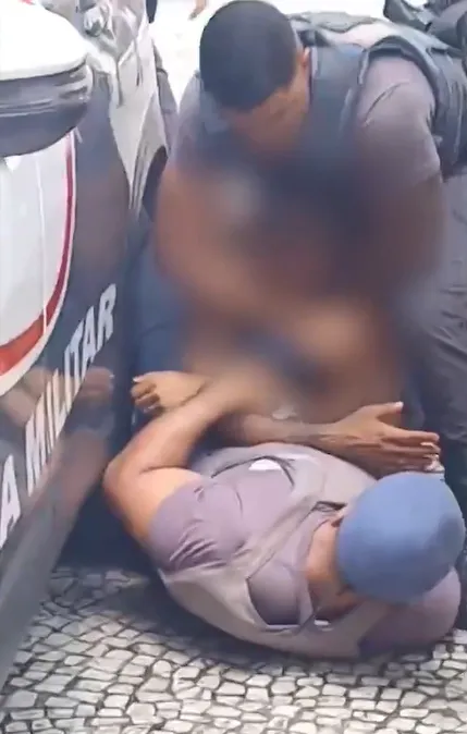Dois policiais tentam imobilizar o homem, que já está caído