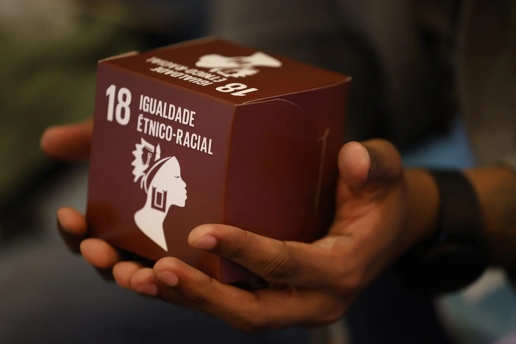 Foto de mão segurando um cubo com o lema do ODS 18