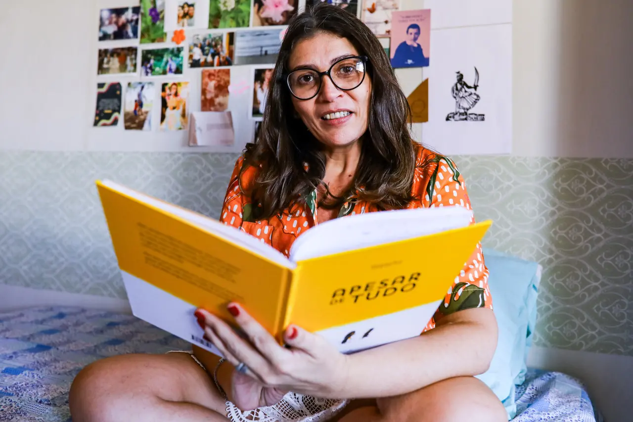 Érica segura livro aberto e olha para a câmera