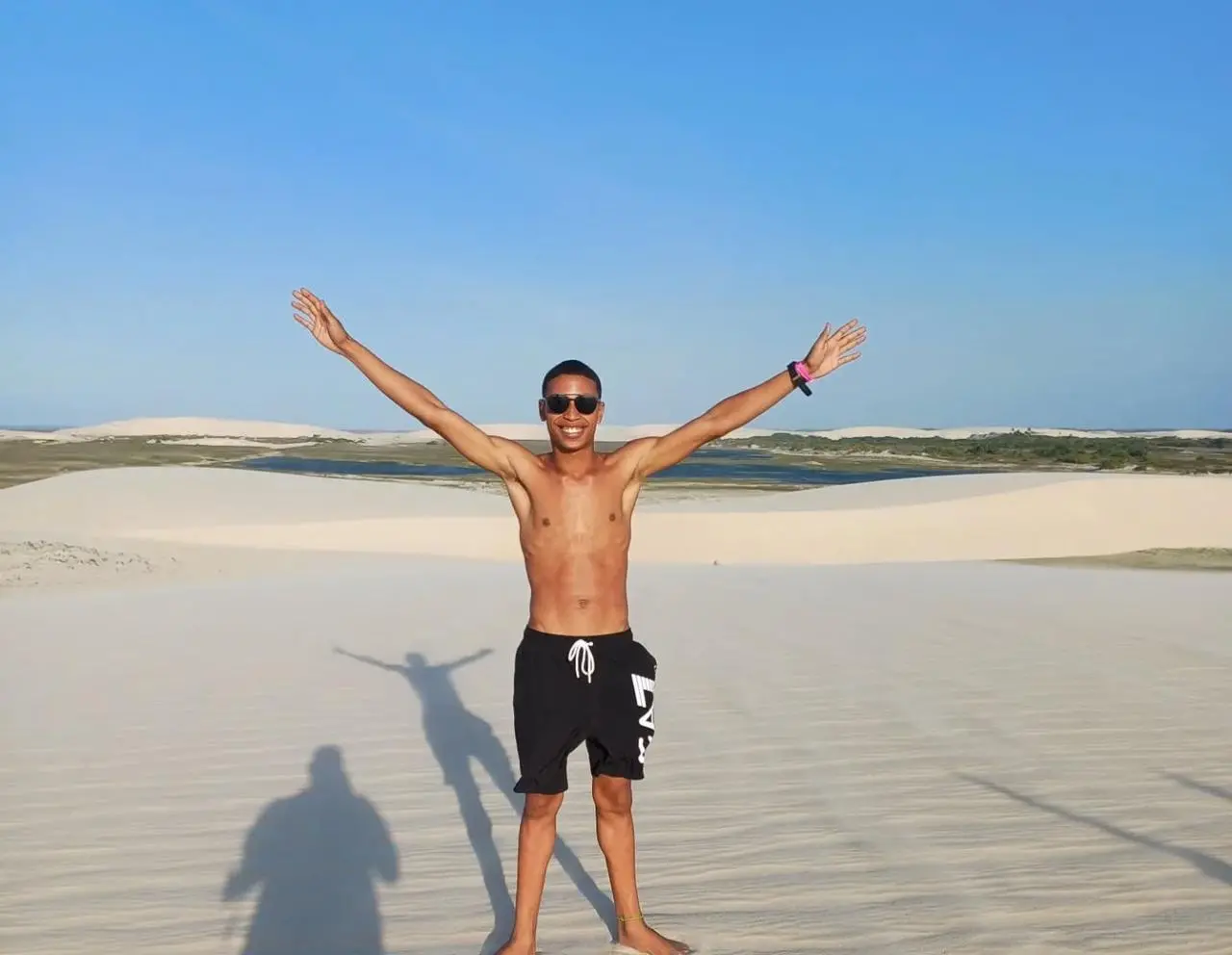 Jovem negro com braços abertos e dunas ao fundo