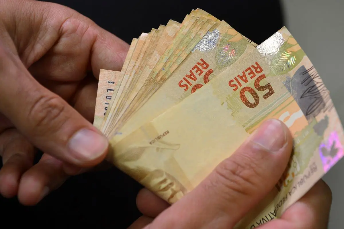 A imagem mostra notas de 50 reais nas mãos de uma pessoa