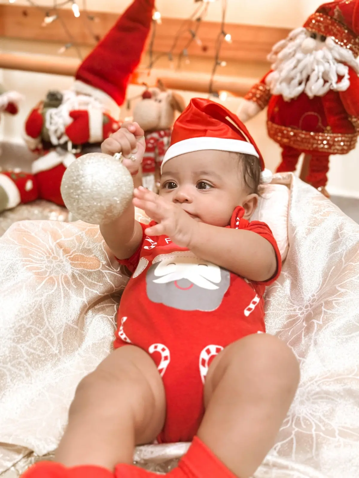 Bebê com gorro de papai noel segurando bolinha de árvore de natal