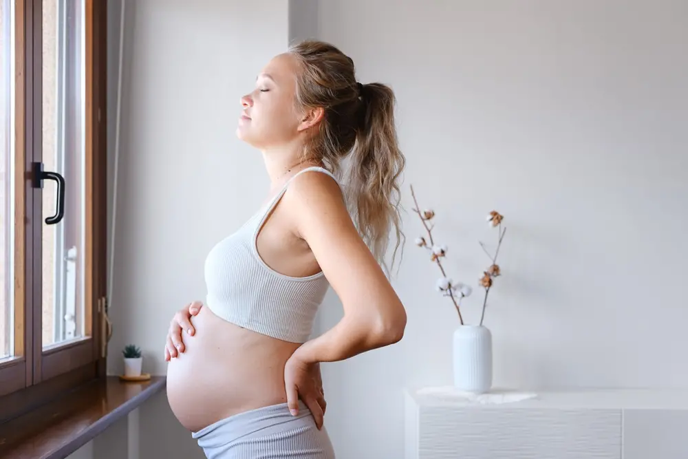mulher grávida põe a mão sobre a barriga e as costas
