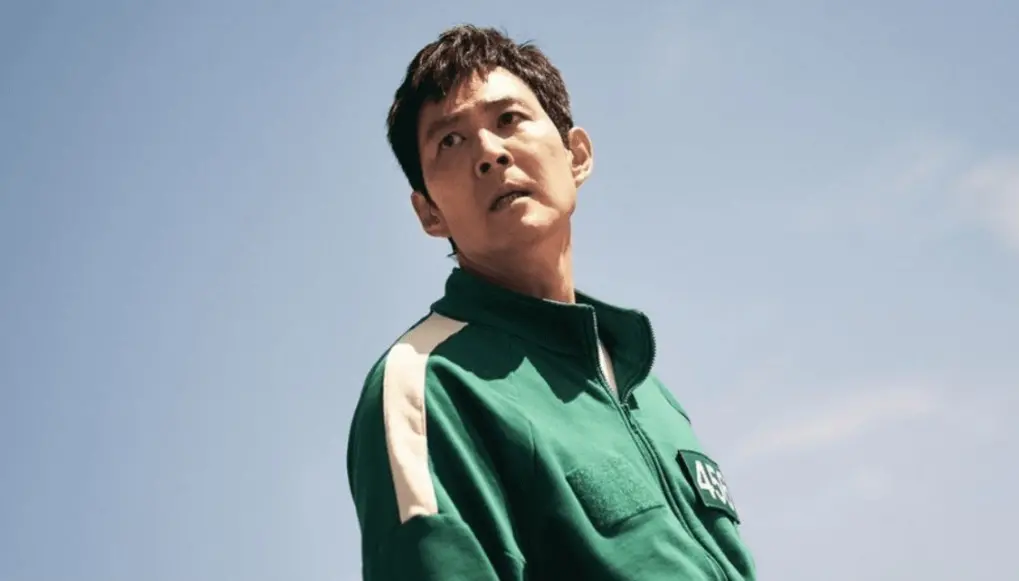 Protagonista de Round 6 observa o horizonte. Ele está vestido com uma roupa verde