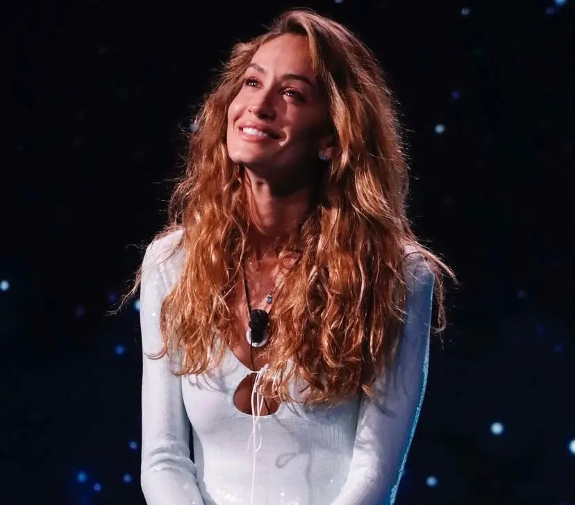 Helena é uma mulher magra, alta e de cabelos longos ondulados e iluminados. Na foto, ela está olhando para cima e sorrindo