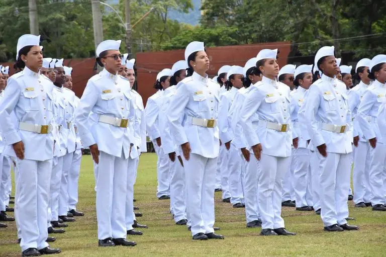 Grupo de mulheres militares em formação, vestidos com uniformes brancos, alinhados e atentos.
