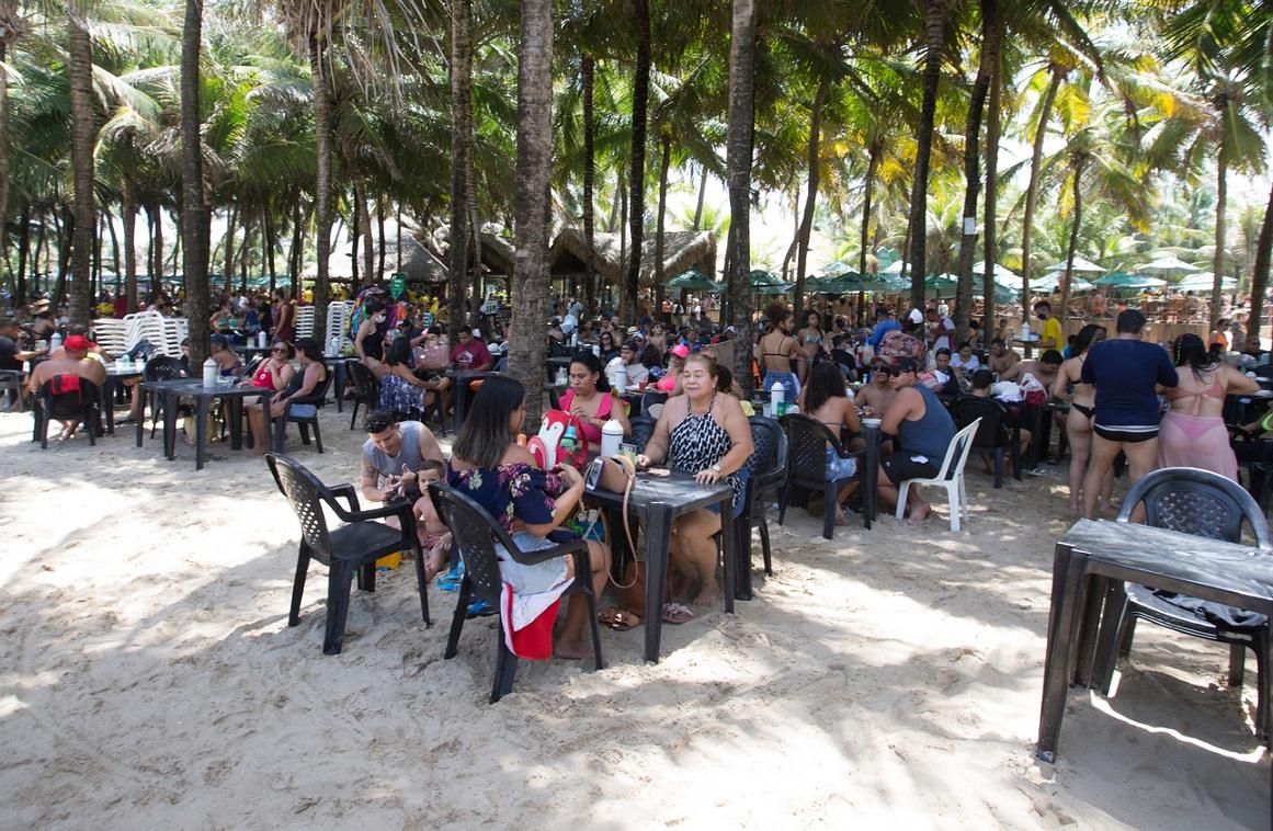 Frequentadores de barraca de praia sentados em mesa perto de coqueiros