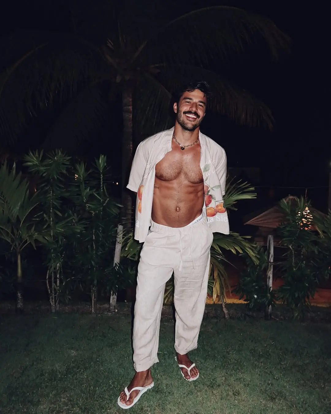 Foto de Mateus Pires, que vai entrar como dupla de Vitória Strada no BBB 25. Na foto, ele está de calça branca e com a camisa desabotoada