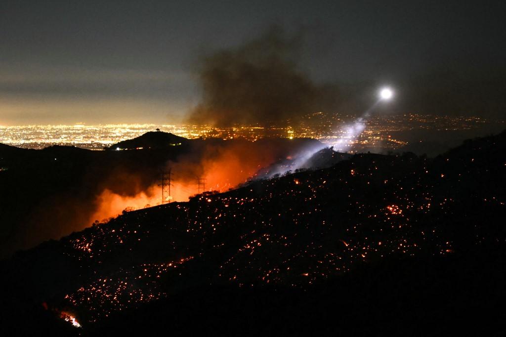 A luz de um helicóptero de combate a incêndios ilumina uma encosta fumegante enquanto o incêndio Palisades cresce perto do bairro Mandeville Canyon e Encino, Califórnia, em 11 de janeiro de 2025.