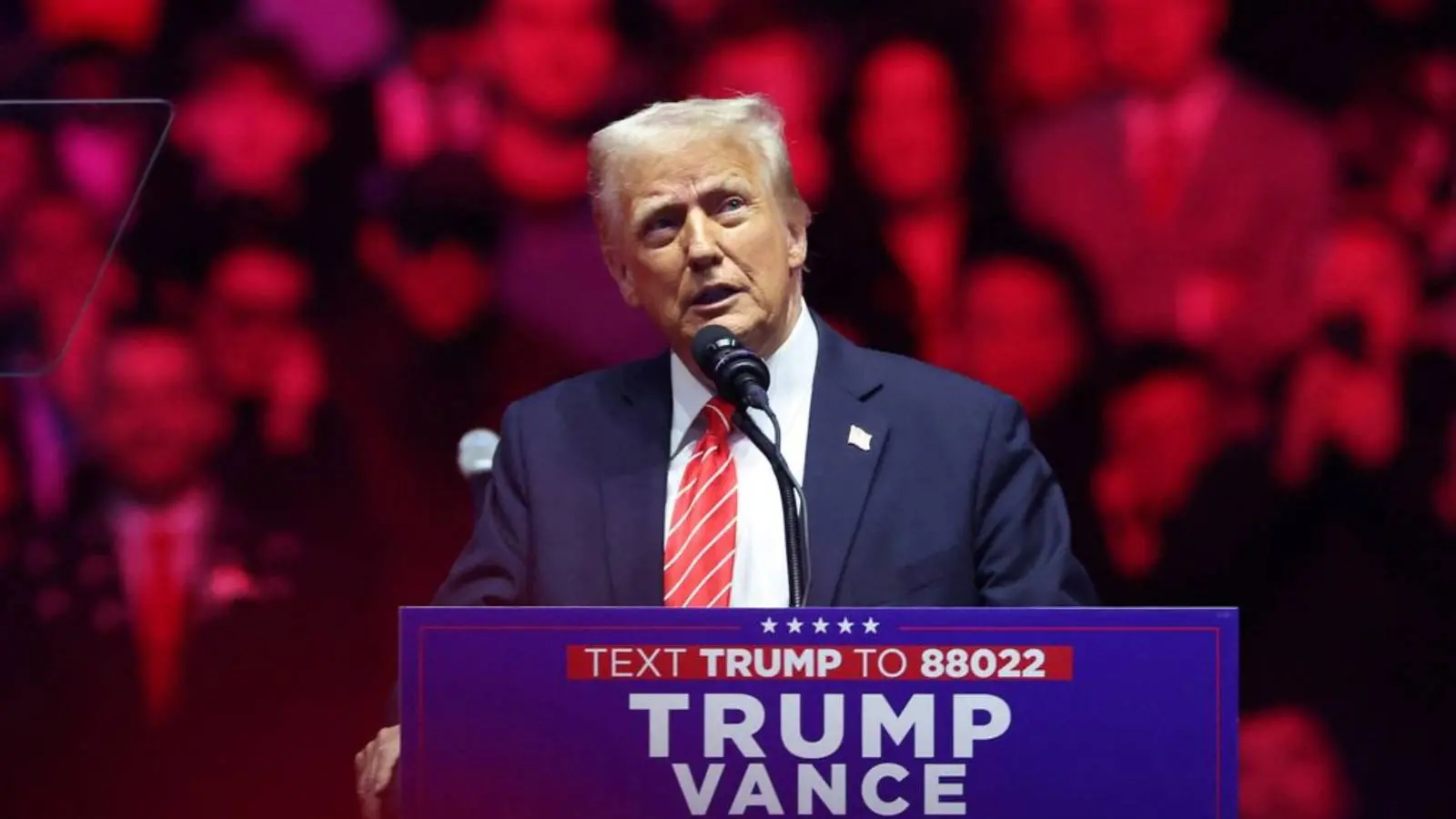 a imagem mostra Donald Trump, empresário a assumir a presidência dos EUA, atrás de um microfone no palco.